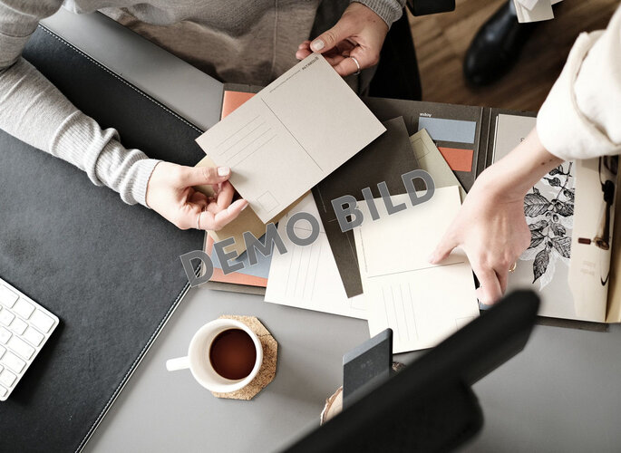 Mehrere Personen betrachten Musterkarten und Druckproben an einem Arbeitstisch.