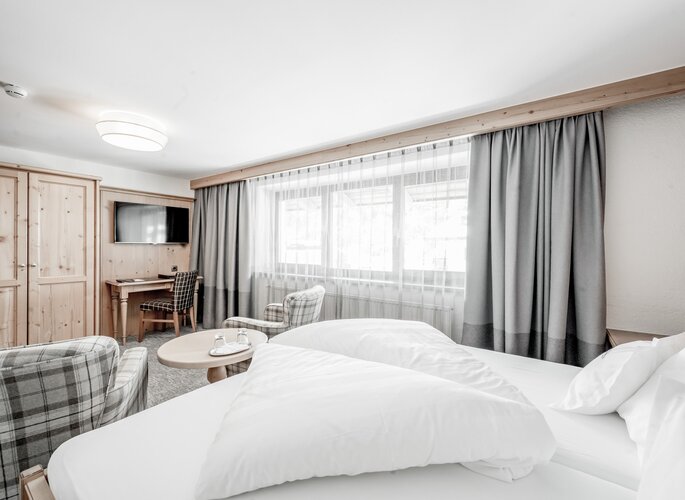 Doppelzimmer im Hotel Jenewein in Obergurgl Helles Doppelzimmer mit Holzmöbeln, zwei Sesseln, TV und großem Fenster im Hotel Jenewein.