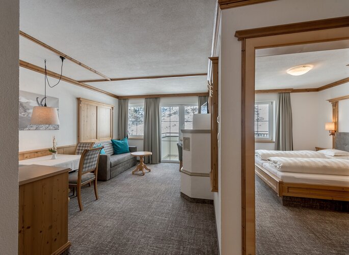 Ein helles Appartement mit Wohnbereich, Esstisch, Schlafzimmer und Blick auf die verschneiten Berge.