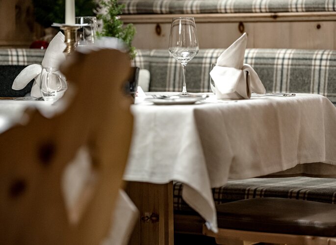 Ein elegant gedeckter Tisch im Hotelrestaurant mit Stoffservietten, Weingläsern und karierten Sitzpolstern.