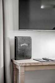 Ein Fernseher und eine schwarze Hotelmappe stehen auf einem Holztisch im Zimmer.