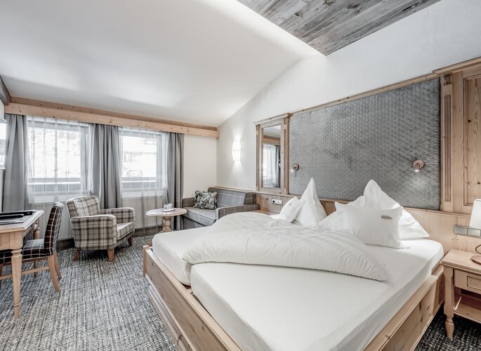 Ein helles Studio mit Doppelbett, Sitzecke und großen Fenstern im Hotel Jenewein.