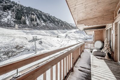 Ein Holzbalkon mit Blick auf die verschneite Berg- und Liftlandschaft.