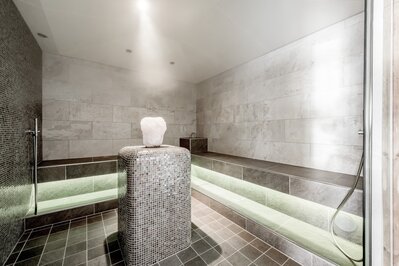 Ein moderner Sauna-Ruheraum mit Sitzbänken und einem beleuchteten Salzelement in der Mitte.