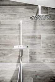 Eine moderne Regendusche vor grauen Wandfliesen im Bad.