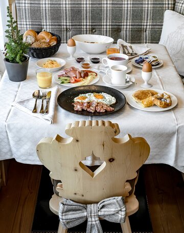 Ein reich gedeckter Frühstückstisch mit Eiern, Aufschnitt, Brot, Müsli und Getränken im Hotelrestaurant.