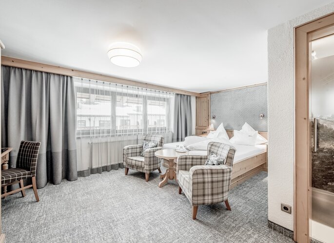 Gemütliches Doppelzimmer im Hotel Jenewein mit Sitzbereich, großen Fenstern und klassischem Ambiente.