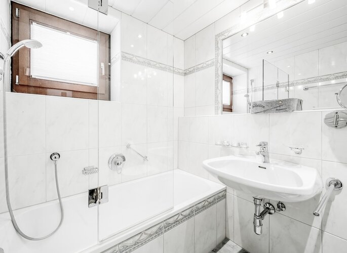 Helles Badezimmer mit Badewanne, Dusche und Waschbecken im Hotel Jenewein.