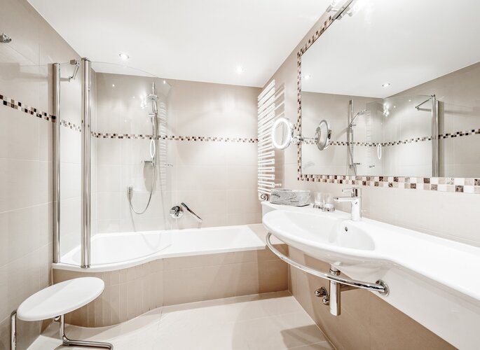 Hotelbad mit Badewanne im Hotel Jenewein Modernes Hotelbad mit Badewanne, Glasduschwand, Waschtisch und großem Spiegel.