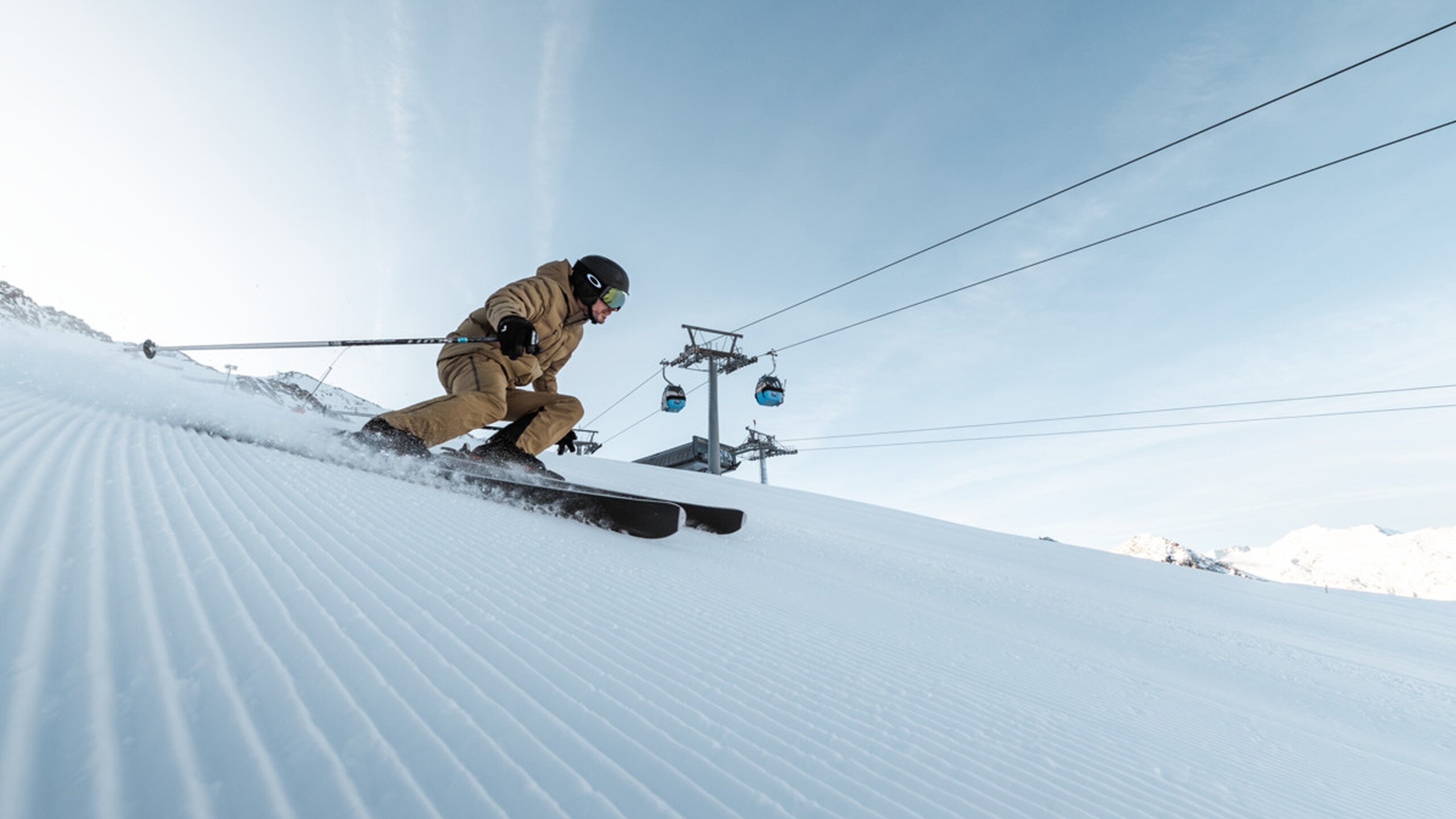 Ein Skifahrer fährt auf einer präparierten Piste unter einer Gondelbahn.
