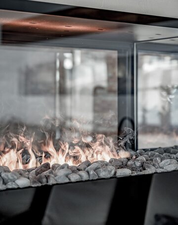 Eine moderne Feuerstelle mit Steinen und sichtbaren Flammen hinter Glas.
