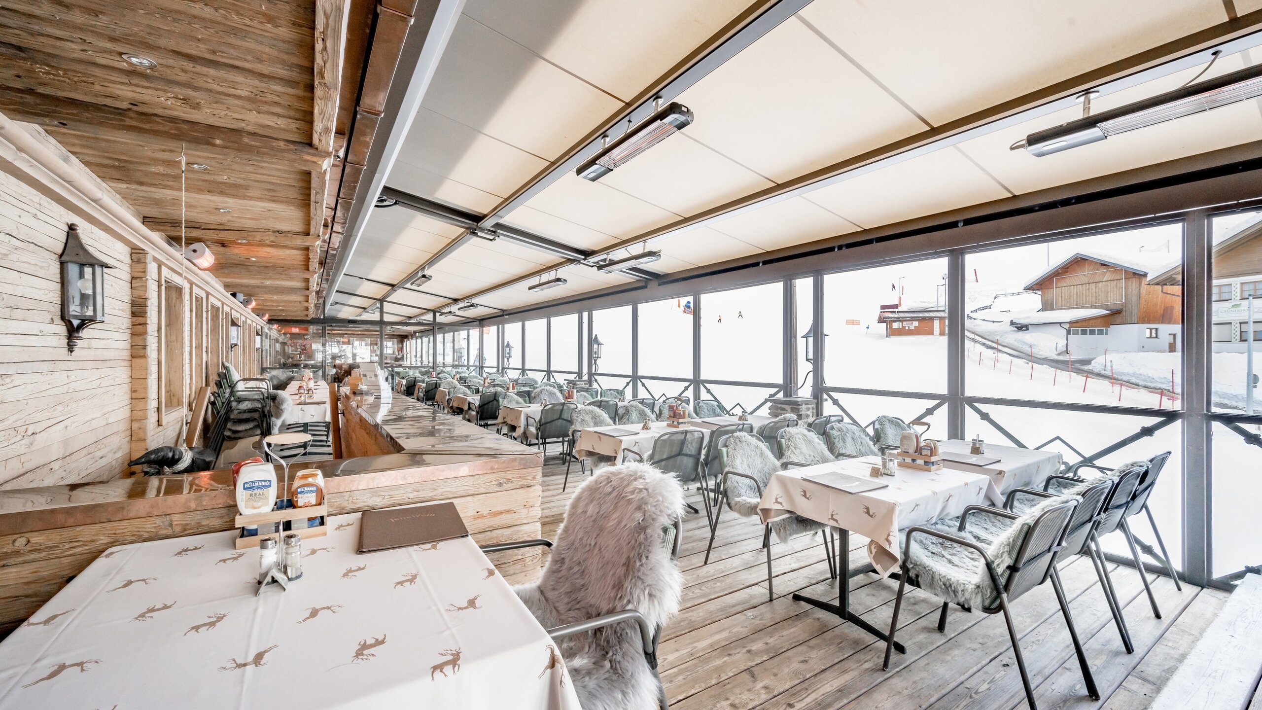 Die überdachte Hotelterrasse mit Tischen und Stühlen bietet Blick auf die verschneite Berglandschaft.