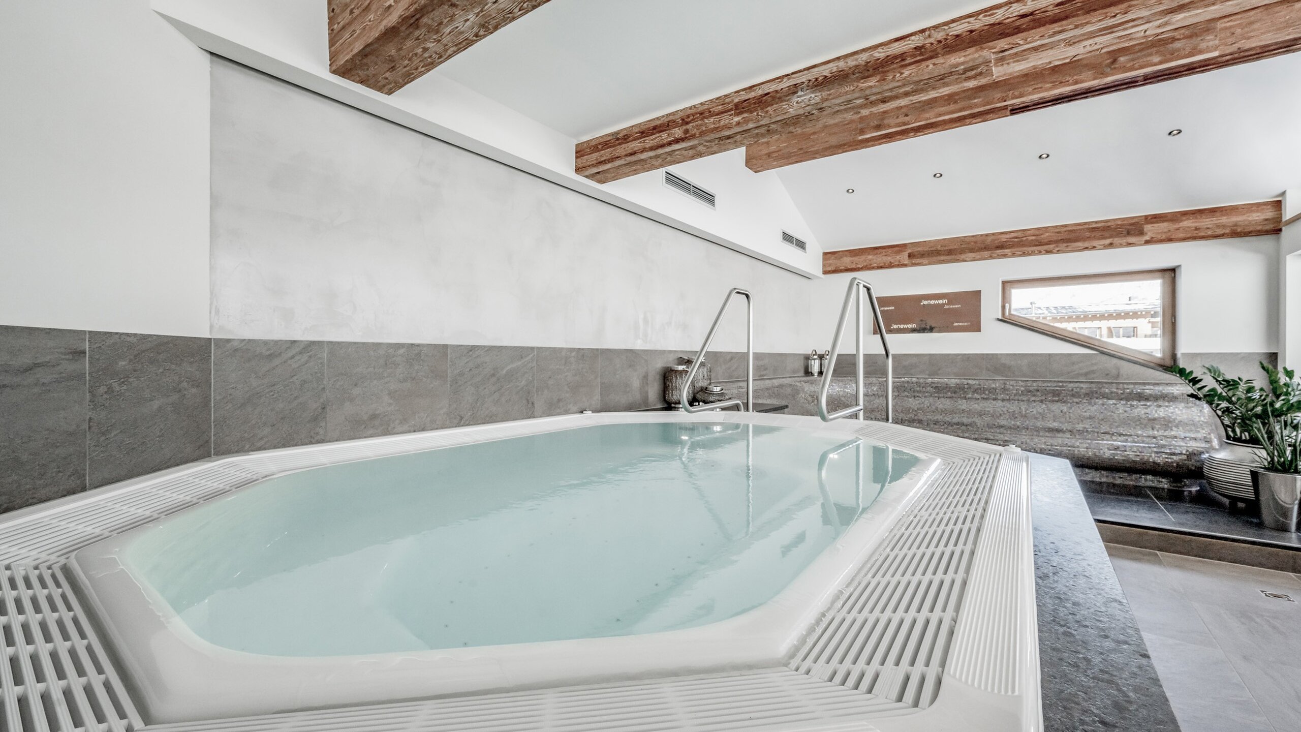 Ein heller Whirlpool im Wellnessbereich des Hotels Jenewein mit Holzdecken und Blick ins Freie.