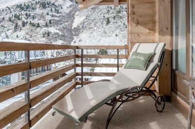 Eine Liege auf dem Holzbalkon mit Blick auf die winterliche Berglandschaft.