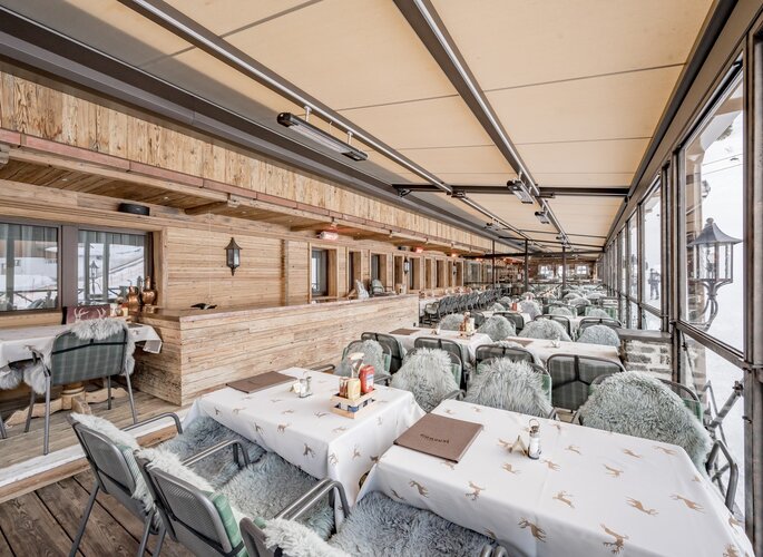 Überdachte Sonnenterrasse mit gedeckten Tischen und Blick auf den Schnee bei Hotel Jenewein.