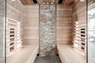 Eine moderne Sauna mit Holzverkleidung, Glasfronten und Steinwand im Wellnessbereich.
