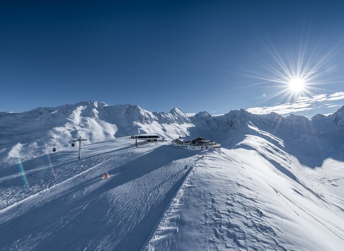 Bergpanorama über verschneiten Skipisten in Obergurgl mit Sonne und Bergstation.