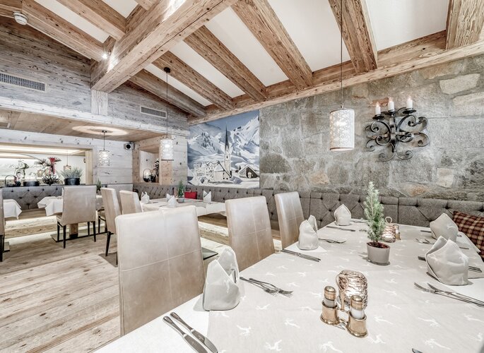 Ein stilvoll gedeckter Restaurantbereich mit Holzbalkendecke, Steinwand und eingedeckten Tischen in der Hexenkuchl.