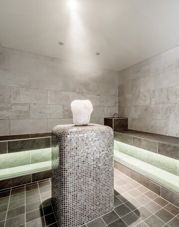 Ein heller Ruhebereich in der Sauna mit gepolsterter Liegefläche und beleuchtetem Sockel.