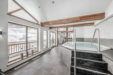 Ein heller Wellnessbereich mit Whirlpool und großen Fenstern mit Blick auf die verschneite Berglandschaft.