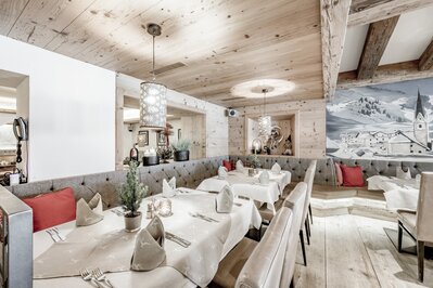 Ein stilvoll gedecktes Hotelrestaurant mit Holzausstattung, Bankettbestuhlung und winterlichem Wandbild.