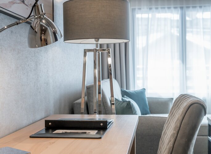 Romantikzimmer im Hotel Jenewein in Obergurgl Ein heller Sitzbereich im Romantikzimmer mit Tischlampe, Schreibtisch und Sofa am Fenster.