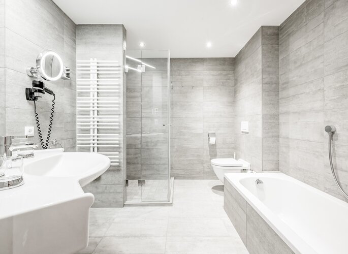 Modernes Hotelbad im Hotel Jenewein Modernes Hotelbad mit Badewanne, Dusche, Waschbecken und Fliesen in hellen Grautönen.