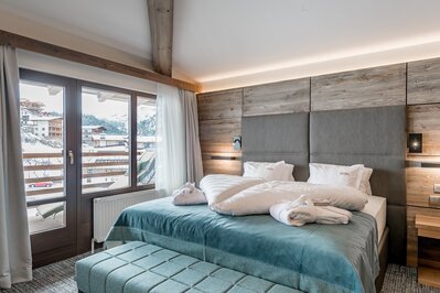 Ein helles Hotelzimmer mit Doppelbett, Holzdetails und Blick auf die verschneiten Berge in Obergurgl.