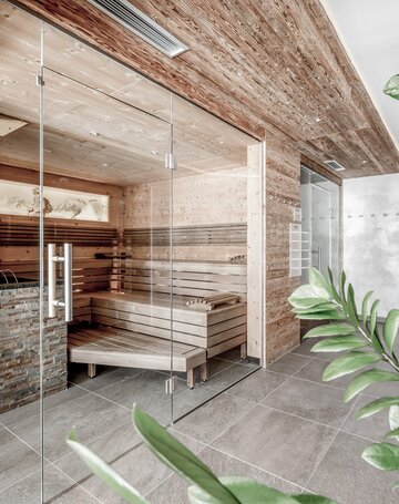 Ein heller Saunabereich mit Holzverkleidung, Glasfront und Liegebank im Hotel Jenewein.