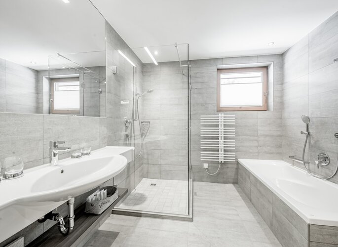 Modernes Familienbad im Hotel Jenewein Modernes Bad mit Badewanne, Dusche, Waschtisch und hellen Fliesen im Hotel Jenewein.