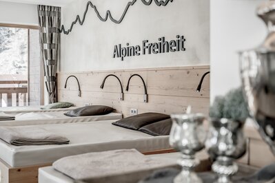 Mehrere Liegen im Ruhebereich mit Blick nach draußen und der Wandbeschriftung "Alpine Freiheit".