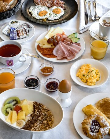 Ein reich gedeckter Frühstückstisch mit Eiern, Aufschnitt, Käse, Obst, Müsli, Saft und Kaffee.