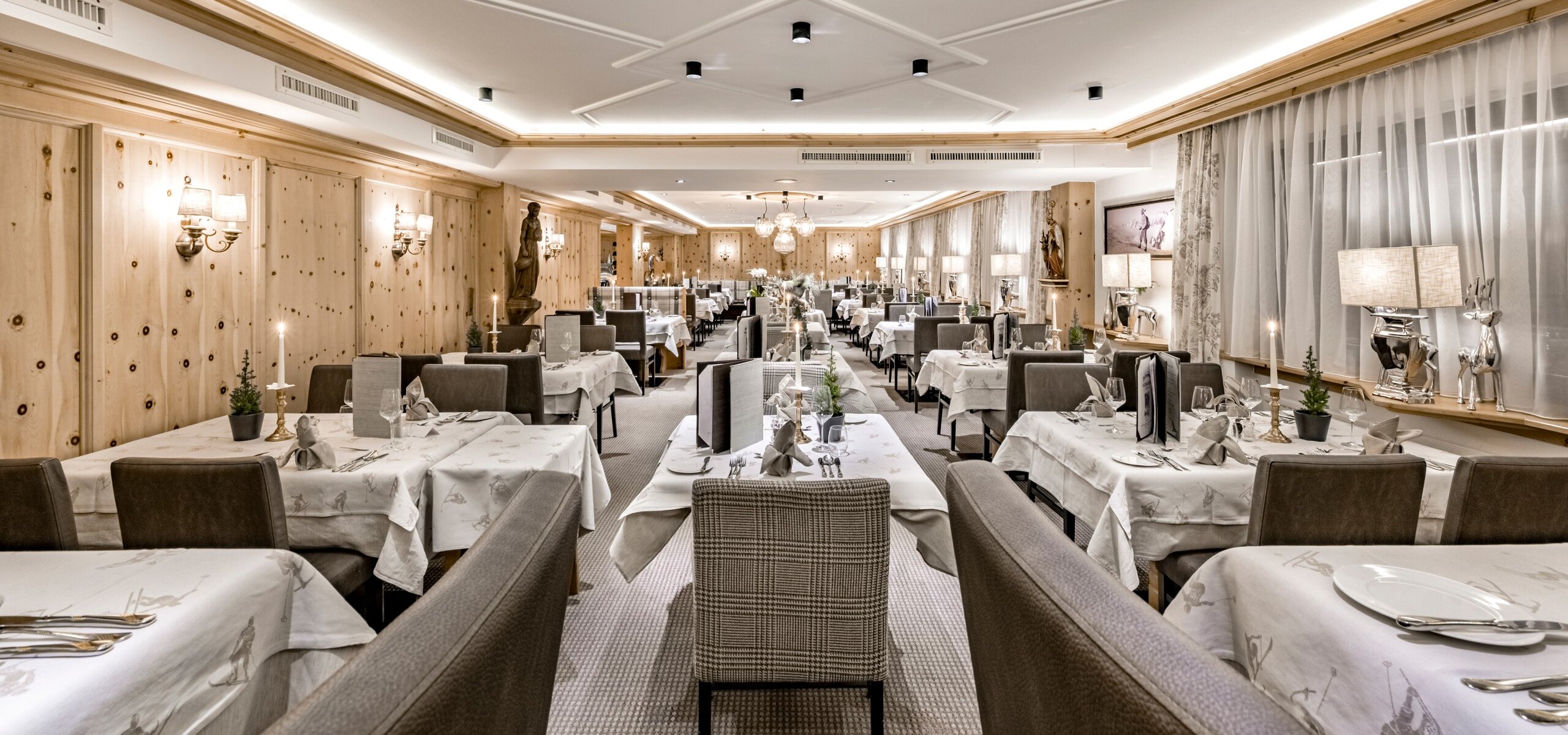 Ein elegant gedecktes Hotelrestaurant mit vielen Tischen, hellen Holzwänden und warmem Licht.