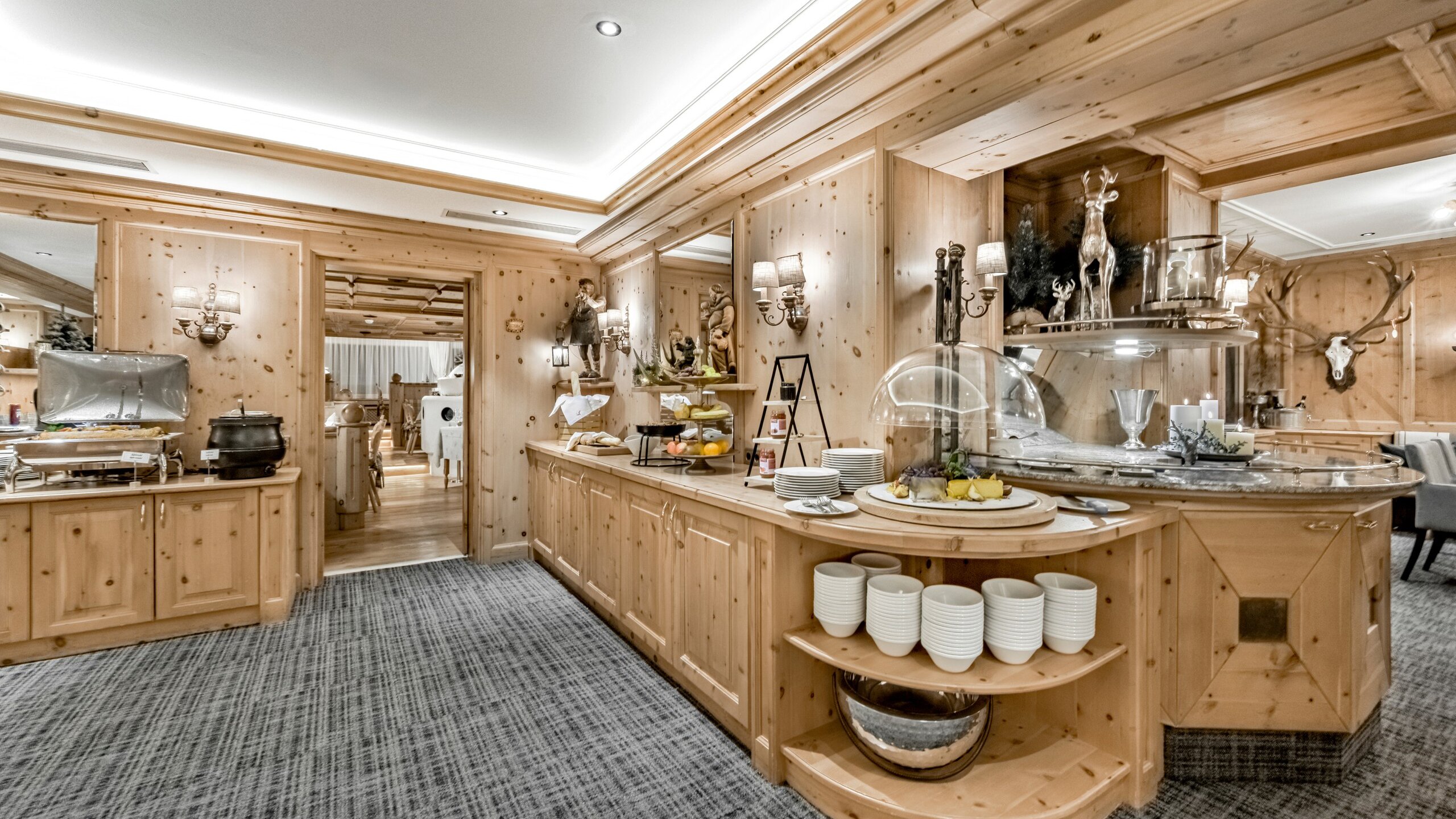 Ein Holzraum mit reich gedecktem Frühstücksbuffet, Geschirr und warmen Leuchten im Hotelrestaurant.