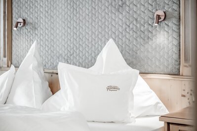 Ein Hotelbett mit weißen Kissen und strukturierter Kopfwand in einem hellen Zimmer.