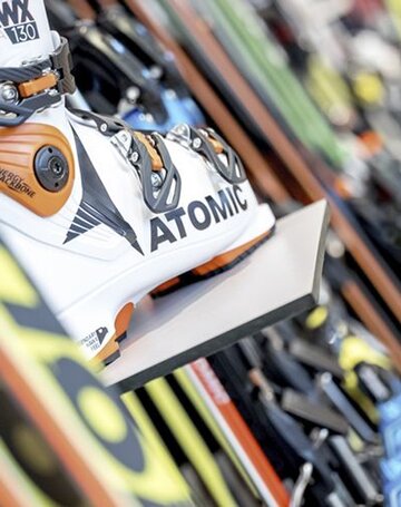 Ein Skischuh von Atomic steht zwischen mehreren Skiern im Verleih.