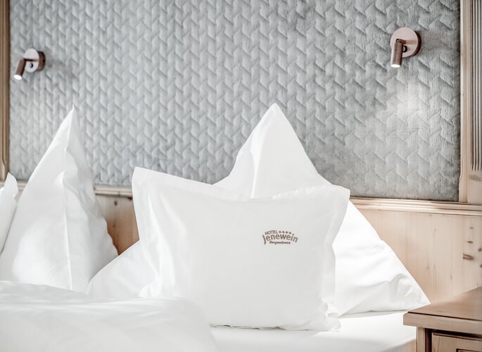 Juniorsuite im Hotel Jenewein in Obergurgl Ein helles Bett in der Juniorsuite mit Kissen im Hotel Jenewein vor einer gepolsterten Wand.