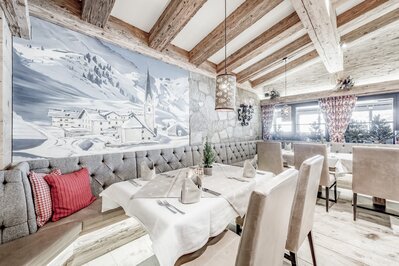 Gemütlich gedeckter Tisch im Hotelrestaurant mit Wandbild einer verschneiten Tiroler Berglandschaft.
