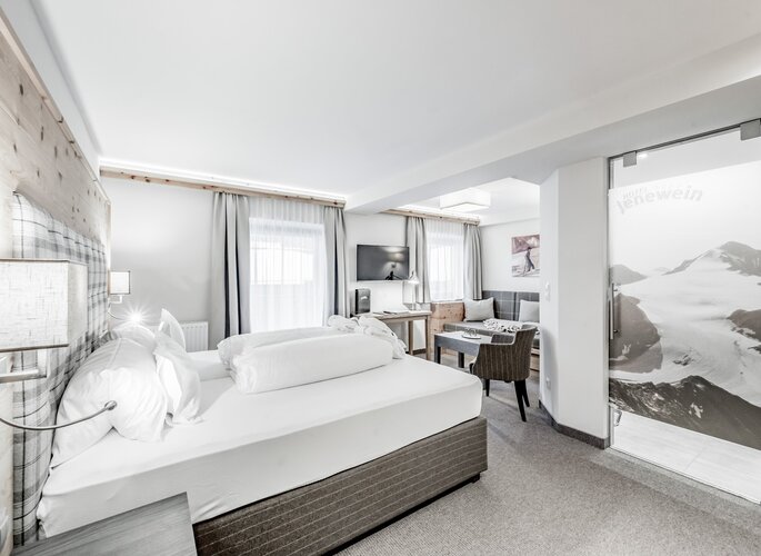 Ein helles Zirbenzimmer mit Doppelbett, Sitzecke und Holzelementen im Hotel Jenewein.