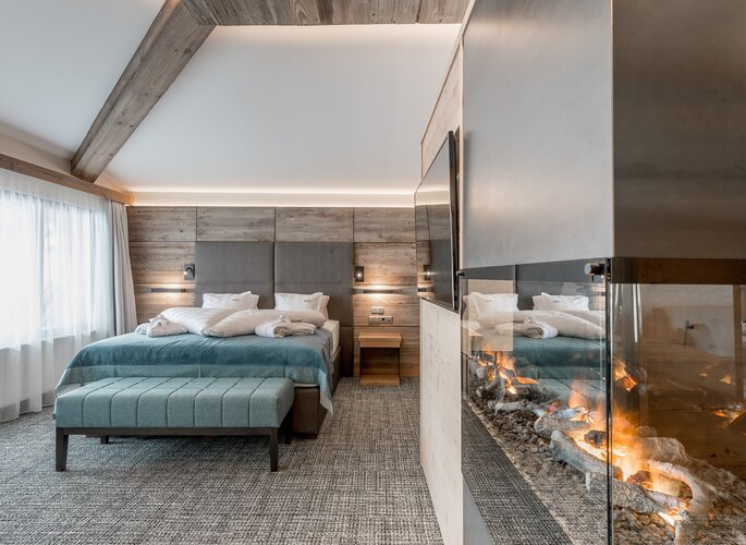 Ein modernes Romantikzimmer mit Doppelbett, Sitzbank und Kamin im Hotel Jenewein.