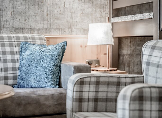 Gemütliche Sitzgruppe im Maisonettenzimmer mit karierten Sesseln, blauem Kissen und Stehlampe.