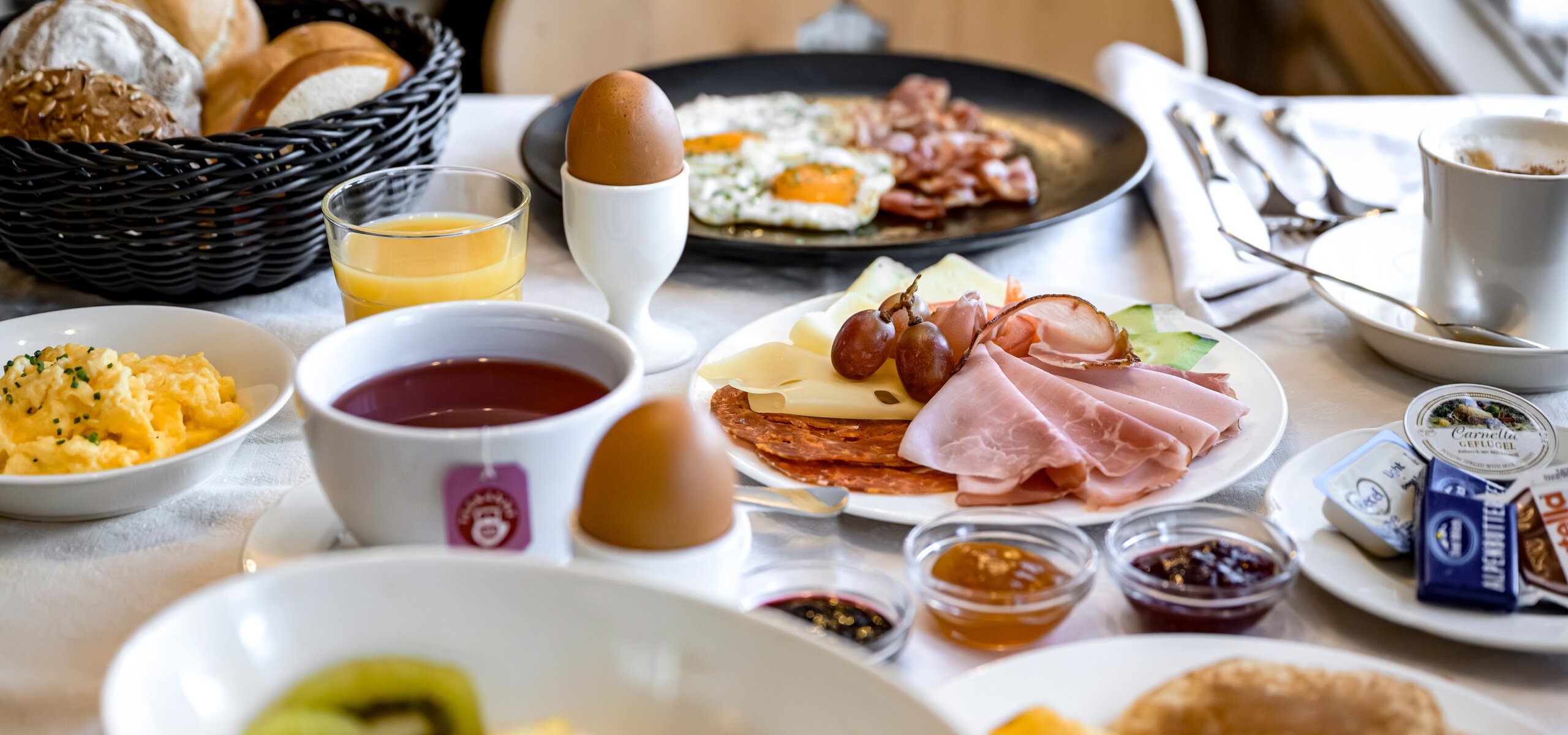Ein reich gedeckter Frühstückstisch mit Brötchen, Aufschnitt, Eiern, Saft und Kaffee im Hotel.