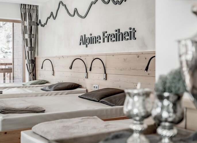 Mehrere Liegen im Ruheraum mit Blick ins Freie und der Wandaufschrift „Alpine Freiheit“.