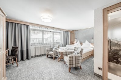 Ein helles Hotelzimmer mit Doppelbett, zwei Sesseln und kleiner Sitzecke.