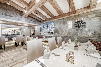 Ein stilvoll gedeckter Speisesaal mit Holzbalken, Steintwand und gedeckten Tischen im Hotelrestaurant.