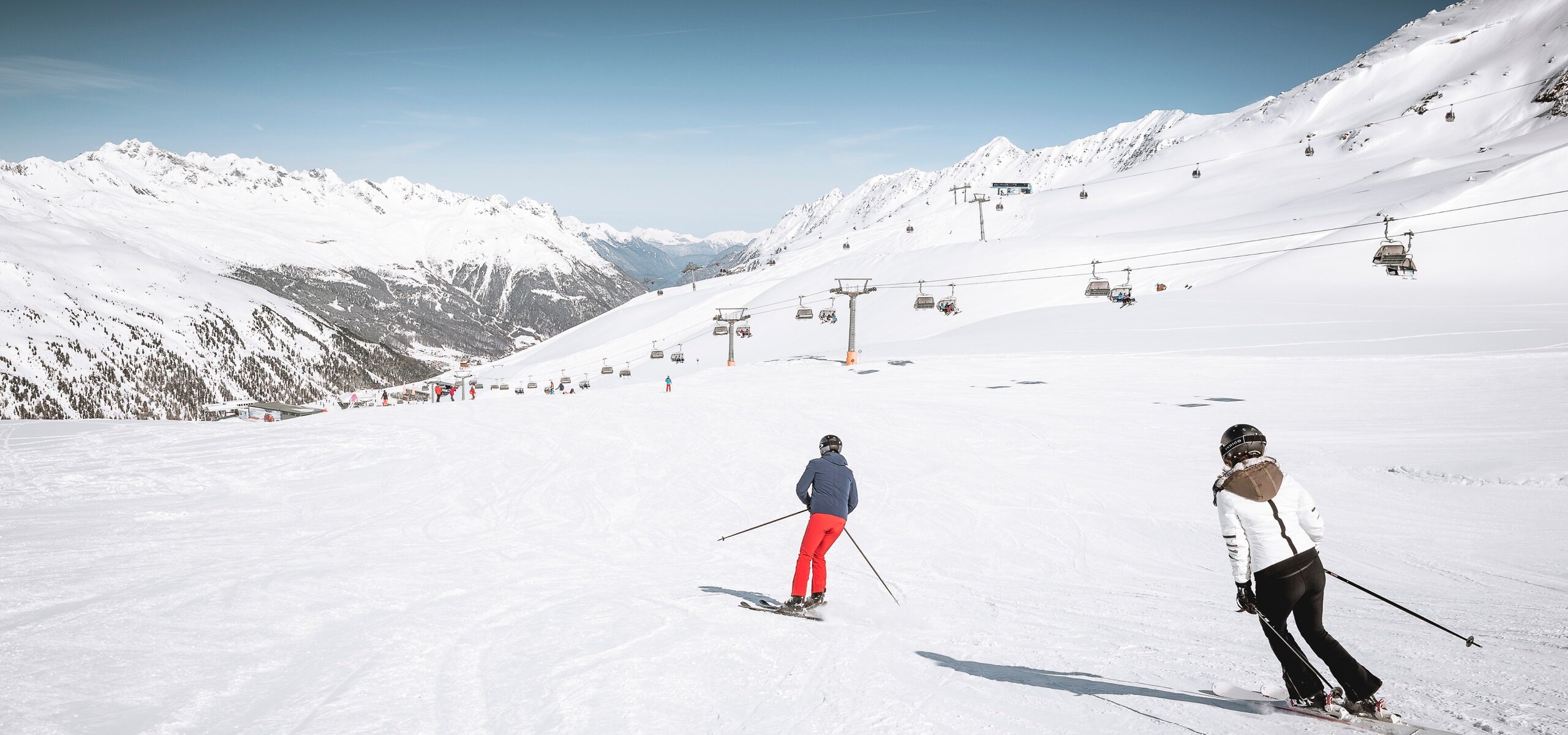 Zwei Skifahrer fahren auf einer breiten Piste im verschneiten Skigebiet Obergurgl bergab.