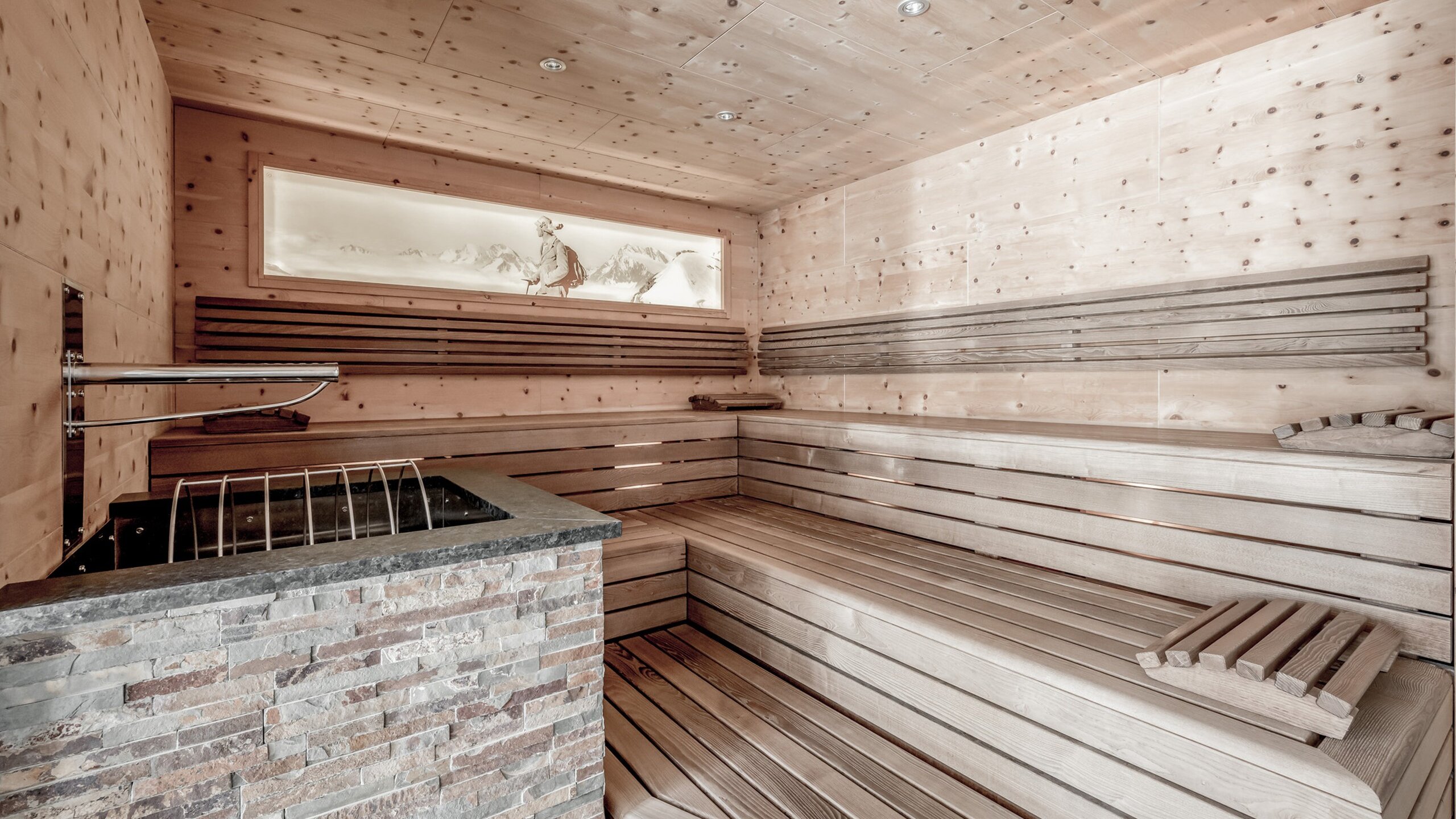 Eine helle Holzsauna mit Steinofen, Sitzbänken und Wandbild im Saunabereich.