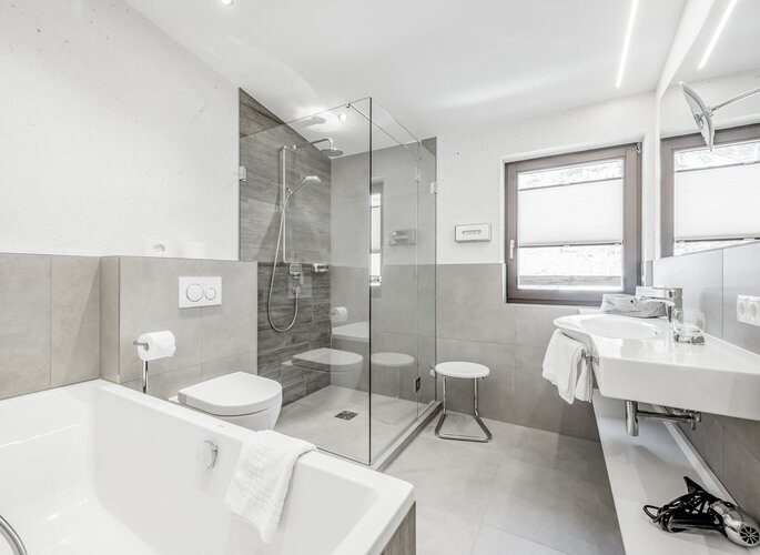Modernes Badezimmer mit Badewanne, Glasdusche, Waschbecken und Fenster im Hotel Jenewein.