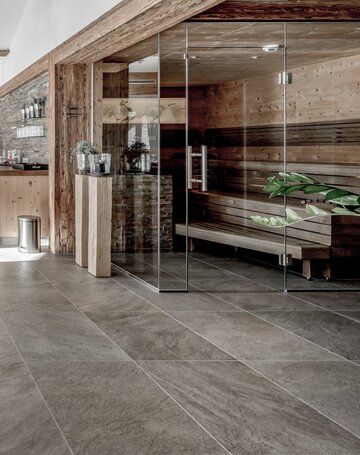 Eine Glasfront trennt die Sauna vom Ruhebereich mit Holzbank und warmen Holzelementen.