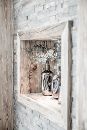 Dekorative Glasvasen mit Zweigen stehen auf einem Holznischen-Regal vor einer hellen Steinwand.